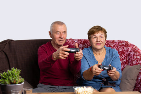 A senior couple is playing a game console with joysticks at home and having fun. Senior online and...
