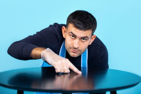 A man in rubber gloves rubs with his finger and checks the cleanliness of the table. A man in an...