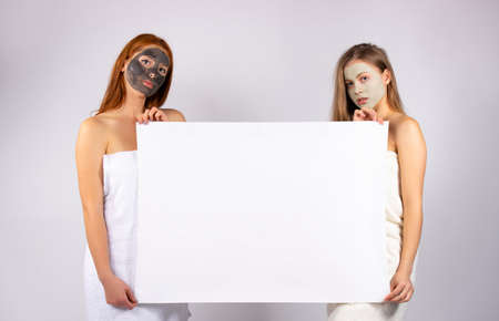 Young girls with facial and with a white banner in hand for advertising. Beauty, spa, health and promotion concept. Photo on white backgroundの写真素材