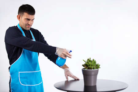 A man pours water on an indoor flower from a spray bottle at home. Housework and gender stereotype concept. Photo on white background with blank spaceの写真素材