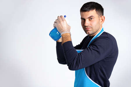 Concentrated man in rubber gloves with a spray in his hands looking at the camera. Gender equality concept. Photo on white background with empty side spaceの写真素材