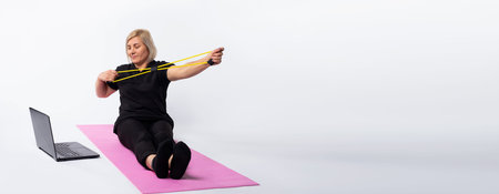 Banner, long format. Fitness at home with a trainer online. An elderly woman sits on a mat in front...