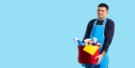 Banner, long format. Close-up of a Caucasian man holding a lot of cleaning products in a bucket against a blue background with blank space. Gender stereotypesの写真素材