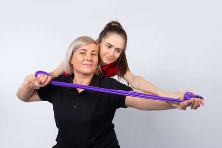 A young girl fitness instructor helps an older woman to do the right exercise. Photo on a white background.の写真素材