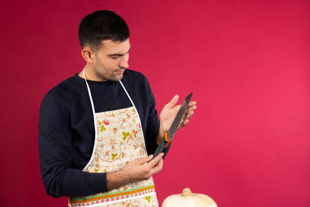 A man holds a kitchen knife in his hands and checks how sharp it is. Photo on a pink background with pusym side space.の写真素材