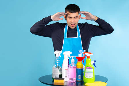 Surprised man from seeing the amount of home cleaning products. Photo on a blue background. The concept of gender stereotypes.の写真素材