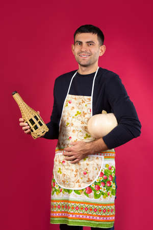 A man smiles after cooking dinner and poses with his chosen drink. The concept of gender stereotypes. Photo on a pink background.の写真素材