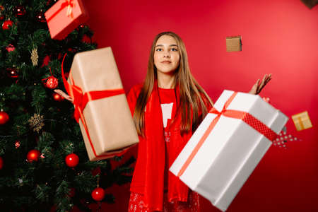 The girl is in pajamas by Xmas tree, with a bunch of gifts in the air. Superhero- women power. Photo on red background.の写真素材