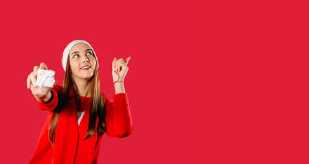 Banner. Girl holds a gift box and points up with a finger. Red background with space for your advertisment.の写真素材