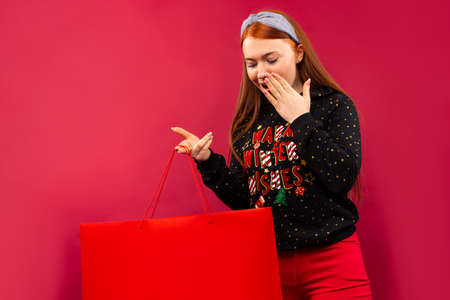 Surprised girl looking into open Xmas gift bag. Isolated on a pink background.の写真素材