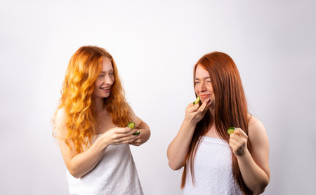 The girls laugh and put pieces of cucumber on their faces. Photo on a white background. Spa and cosmetology concept. High quality photoの写真素材