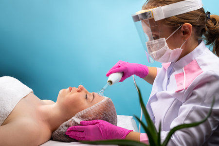 The cosmetologist performs cosmetic procedures with darsonval for a young client. Spa and beauty in...