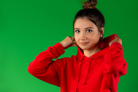 An attractive brunette girl with brown eyes in a red body shirt on a green background looks cute at the camera. High quality photoの写真素材