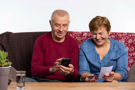 An older couple pays by phone and credit card for ordering products by courier. Pandemic and online delivery concept. High quality photoの写真素材