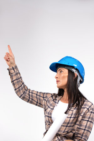 Woman architect in hard hat looks up and points up with index finger. Place for advertising. White background. High quality photoの写真素材