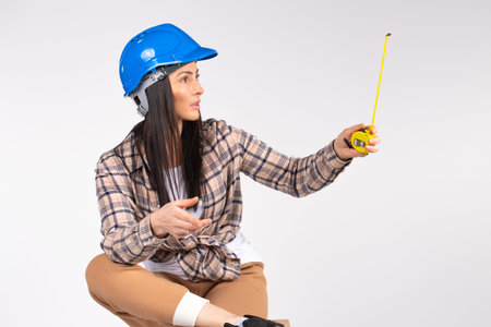Handywoman with tape measure on white background looks to the side. Space for advertisment. High quality photoの写真素材