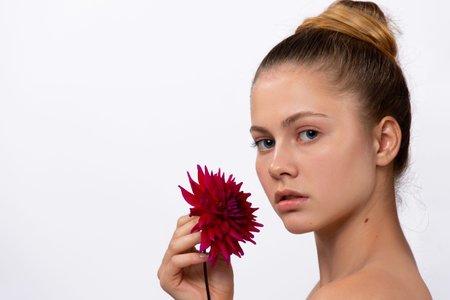 Cute girl model with a burgundy color flower in her hand, posing on a white background. Side space....