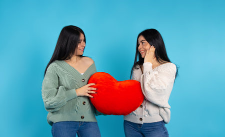 Twin girls with a big red heart in their hands. Blue background. Valentine's day, charity and giving back concept. High quality photoの写真素材