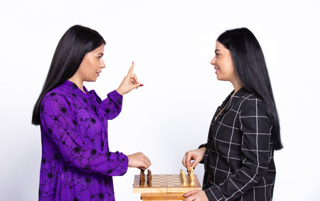 Twins play chess on a white background. One of the girls points to the top, her first move. Black and white game concept. High quality photoの写真素材