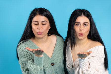 Beautiful caucasian twin girls blow a kiss to the camera. Blue background. High quality photoの写真素材