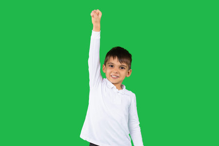Funny caucasian boy in white shirt holds his fist up for victory and solidarity on a green...