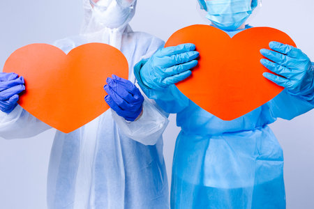Cropped photo of two doctors in pandemic uniform holding big red hearts. St Valentine's Day at work,...