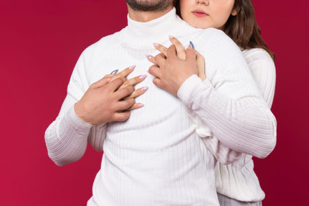 Red background. Enlarged photo of an embrace where girl's hands hug man in a white sweater. Love on...