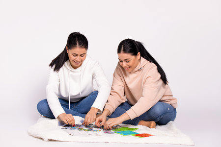 Twin girls enthusiastically collect a puzzle on the floor. An interesting pastime.の写真素材