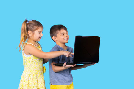 Happy children are smiling and sitting at the laptop. Blue background. Pastime. Technologies. Childrens emotions.の写真素材