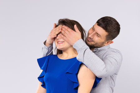 A man covers eyes with his hands to a young girl on a gray background. Surprise on Valentines Day.の写真素材