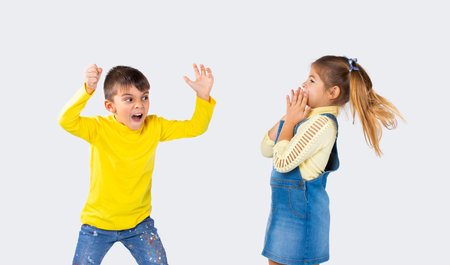 Preschool boy scares his girlfriend on a white background. The concept of emotions and the time spent by children.の写真素材