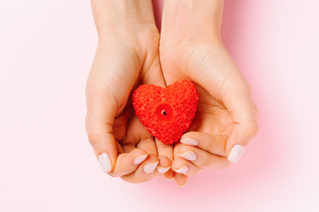 Female hands with gentle manicure hold a heart-shaped candle. Pink background and St.Valentines day...