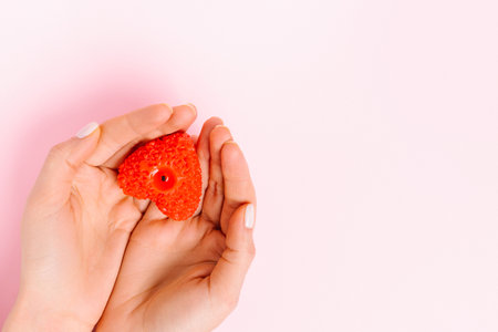 Hands hold a heart-shaped candle. Pink background and empty side space where your ad could be. Valentines Day, charity.の写真素材