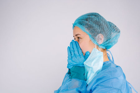 Profile photo. A frustrated young nurse has removed protective mask and pray for life hope. Side space. Gray background.の写真素材