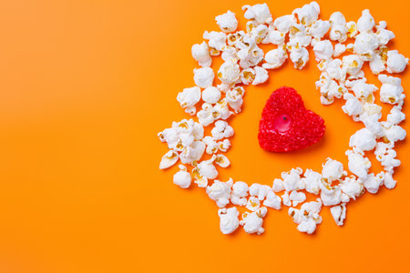 Popcorn and a candle in the shape of a red heart on orange background with blank space.の写真素材