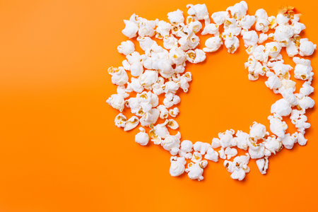 Scattered popcorn in the shape of heart on orange background. Time spent by loved ones. Movie and popcorn.の写真素材
