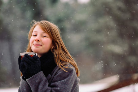 A satisfied red-haired girl with a red nose in a winter forest warms up with fragrant hot tea....