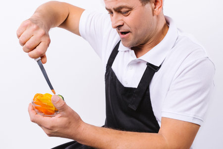 Enlarged photo of a male cook in a black apron with a bowl of vegetables and a knife on a white...