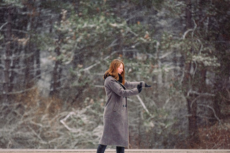 A young girl in a gray coat is keen on photography. Taking pictures of the winter forest and...