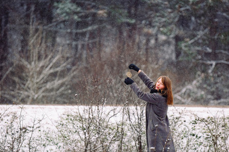 Landscape of an abandoned forest in the snow. A young girl is broadcasting something to a small fragile tree and looking at the camera.の写真素材