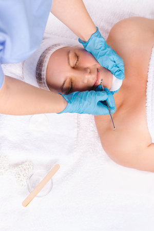 Deep facial cleansing of a womans face with the hands and UNO spoon of a beautician in gloves. In the salon on a white towel. Cosmetologist using mechanical instrument spoon uno removing blackheadsの写真素材