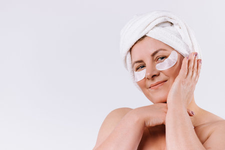 Contented senior woman posing against a white background with a towel on her head and pads under her...