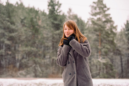 A girl with a sweet smile in frosty weather against the background of a forest with tall trees....