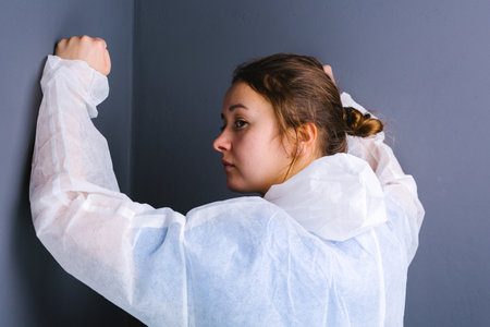 Photo of a tired female doctor who rested her fists against a gray wall and looks away. Photo from behind.の写真素材