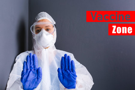 A young doctor in protective equipment and medical goggles shows stop with both hands against the...