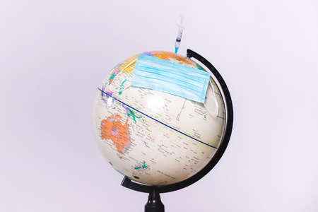 Big globe, medical mask and vaccination syringe. Global coronavirus pandemic concept on white background with side space.の写真素材