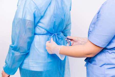 Enlarged photo of the hands of a nurse tie a disposable gown to a patient preparing for hospitalization.の写真素材