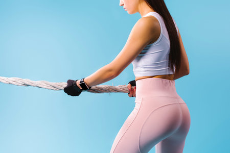 Cropped photo of a girl with pumped up buttocks pulling a rope on a blue background.