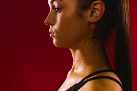 An enlarged profile photo of a caucasian girl sweating after physical exertion against a red background. Dark photo of real brunette womanの写真素材