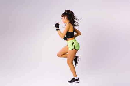 A girl in shorts and a top with headphones runs in place on a white background. Photo full length....
